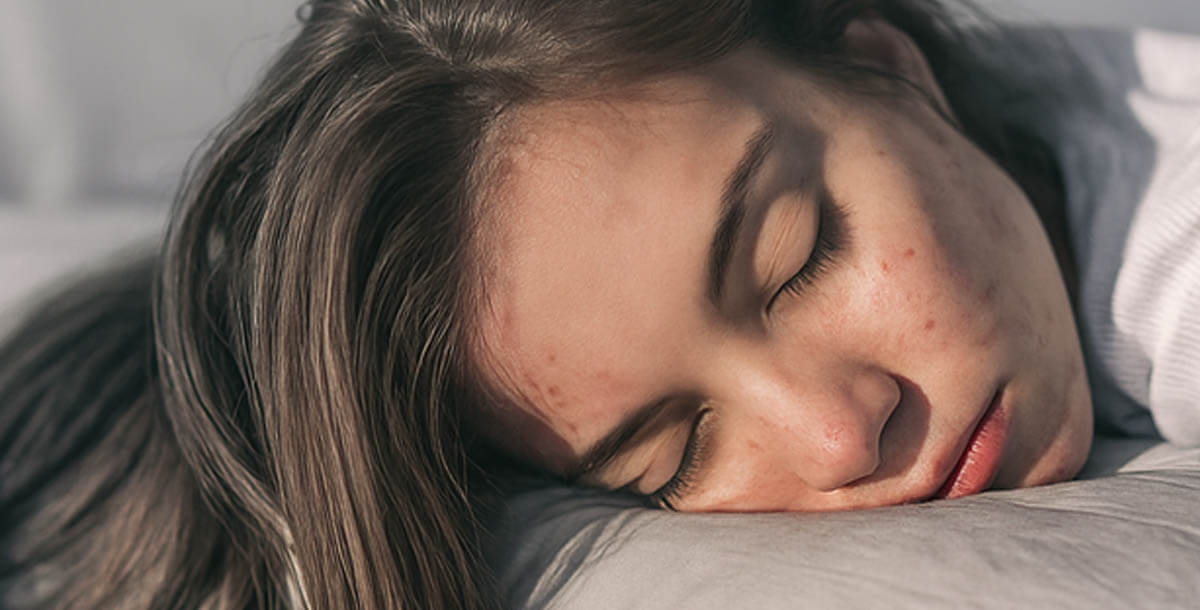 Woman looking at tired skin in mirror after sleeping
